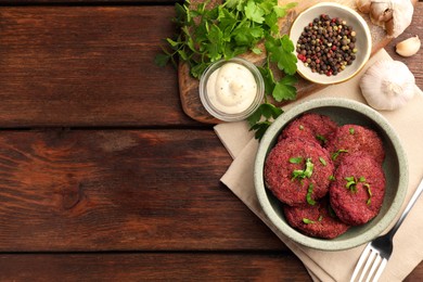 Tasty vegan cutlets with sauce and ingredients on wooden table, flat lay. Space for text