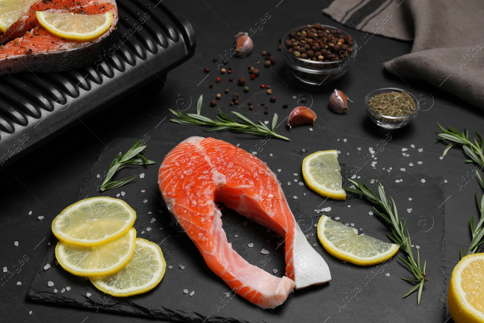 Photo of Cooking salmon. Grill, fresh fish steaks, lemon and spices on dark table