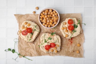 Photo of Delicious sandwiches with hummus and ingredients on white tiled table, flat lay