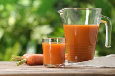 Photo of Glass and jug of carrot drink on table against blurred background, space for text