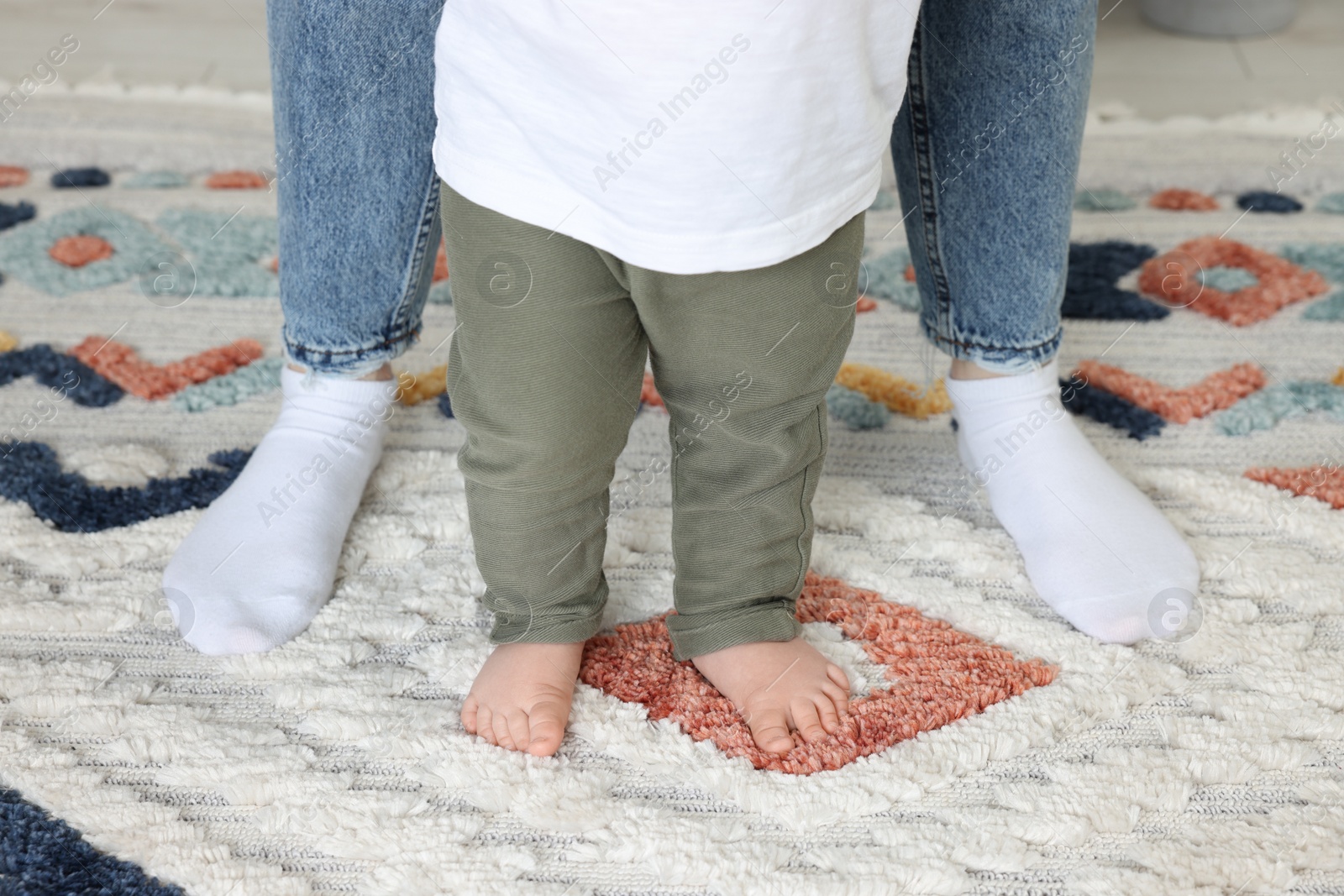 Photo of Mother supporting her son while he learning to walk on carpet indoors, closeup