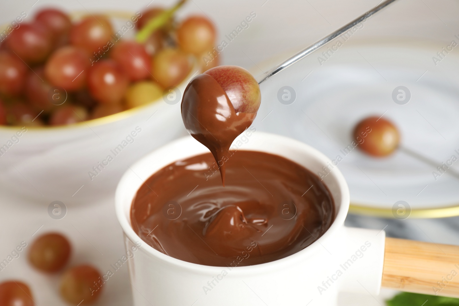 Photo of Fondue pot with chocolate and grape on table, closeup