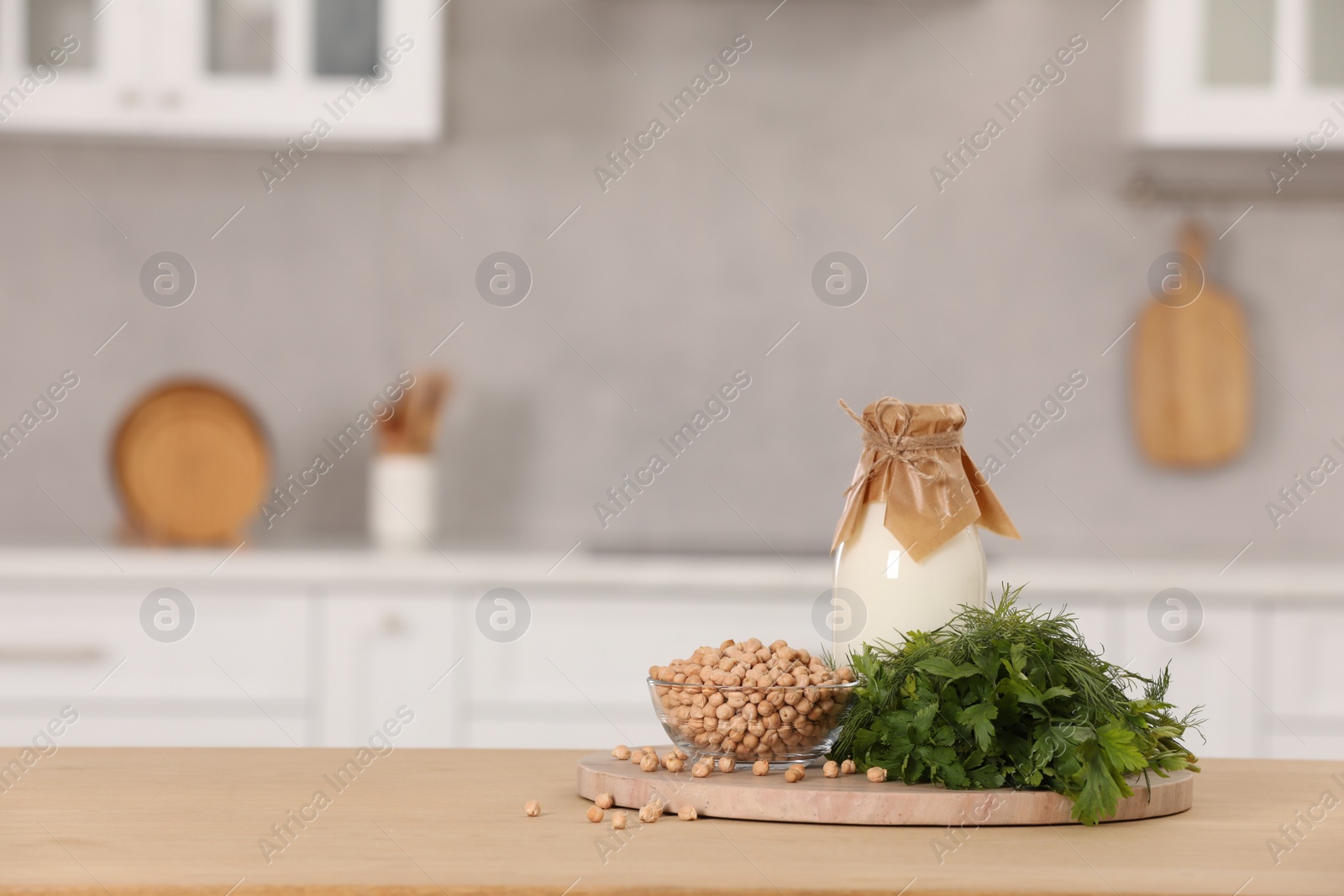 Photo of Bottle with milk, chickpeas and herbs on table in kitchen. Space for text