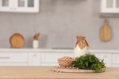 Photo of Bottle with milk, chickpeas and herbs on table in kitchen. Space for text