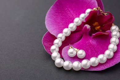 Photo of Elegant pearl earrings, bracelet and orchid flower on black background, closeup. Space for text