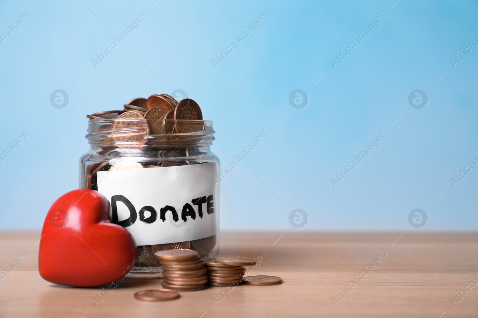 Photo of Red heart and donation jar with money on table against color background. Space for text