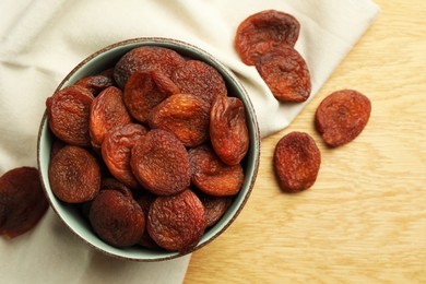 Tasty apricots with bowl on wooden table, flat lay. Dried fruits