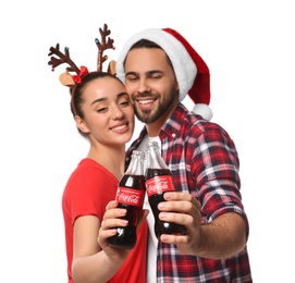 MYKOLAIV, UKRAINE - JANUARY 27, 2021: Young couple holding bottles of Coca-Cola against white background, focus on hands. Christmas atmosphere