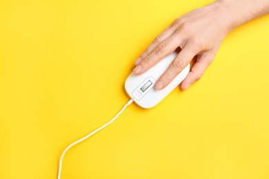 Photo of Woman using modern wired optical mouse on yellow background, top view
