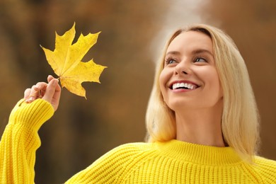 Portrait of happy woman with autumn leaf outdoors