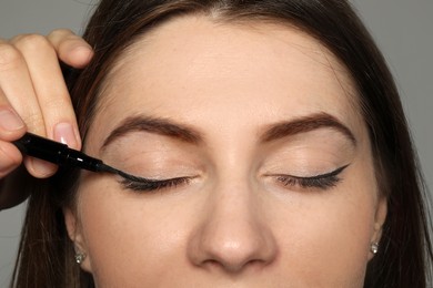 Artist applying black eyeliner onto woman's face on grey background, closeup