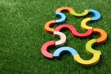 Photo of Colorful wooden pieces of play set on green grass, closeup with space for text. Educational toy for motor skills development