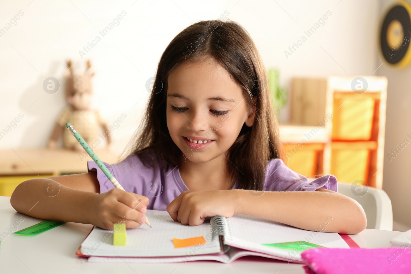 Photo of Little girl doing homework at table indoors