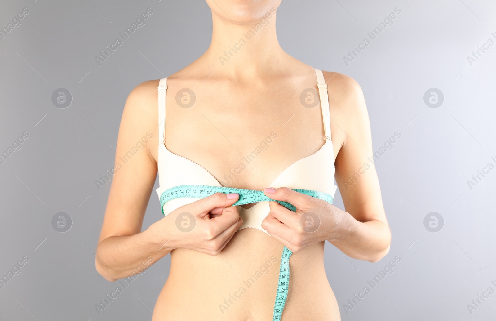 Photo of Young woman measuring breast size on gray background, closeup. Cosmetic surgery