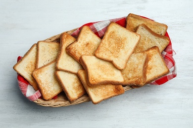 Photo of Basket with toasted bread on white wooden table, top view