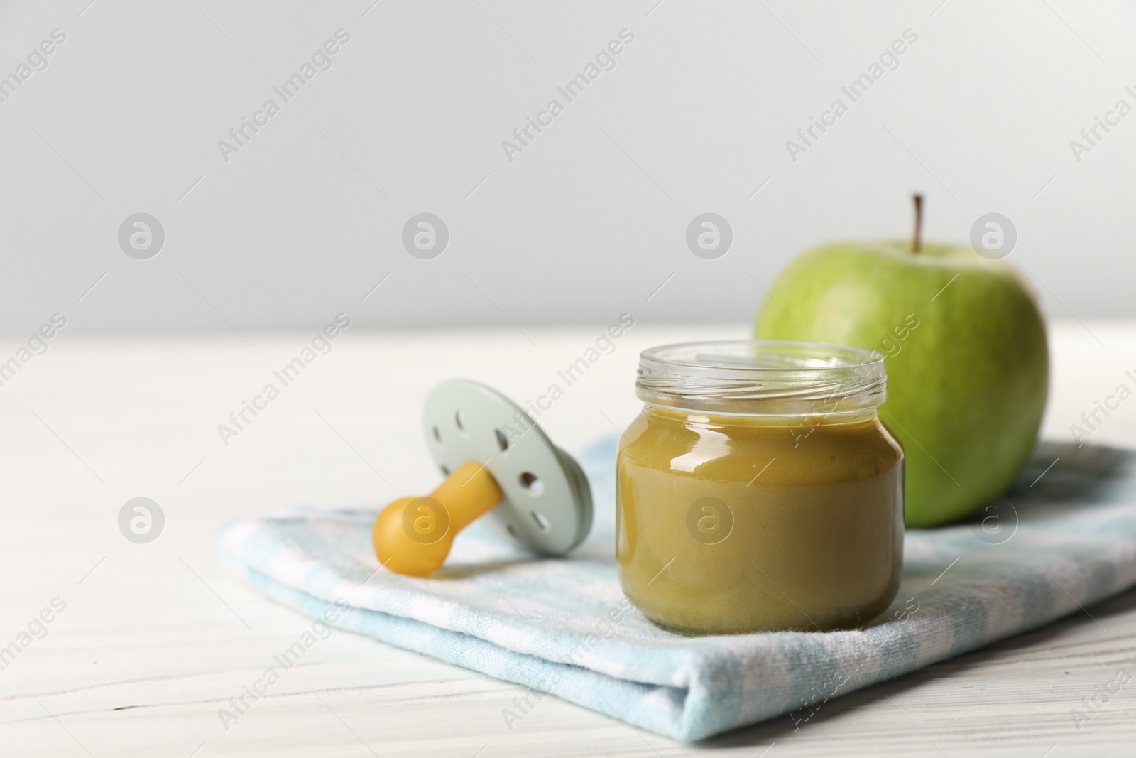 Photo of Jar with healthy baby food, apple and pacifier on white wooden table. Space for text