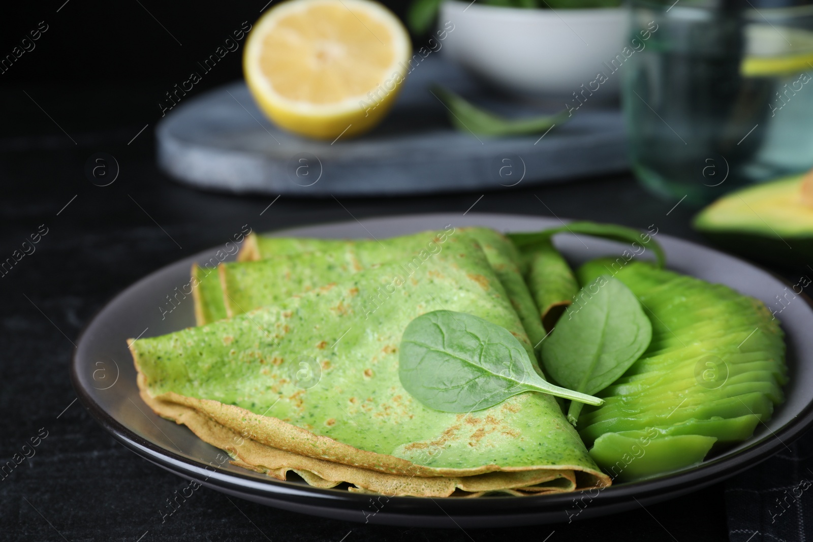 Photo of Delicious spinach crepes with avocado on black table, closeup