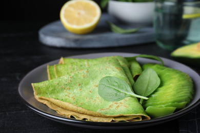 Delicious spinach crepes with avocado on black table, closeup