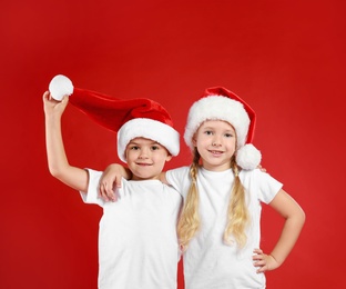 Photo of Cute little children wearing Santa hats on red background. Christmas holiday