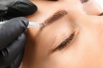Photo of Young woman undergoing eyebrow correction procedure in salon