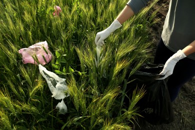 Photo of Woman with trash bag collecting garbage in wheat field, closeup
