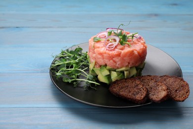 Photo of Tasty salmon tartare with avocado, microgreens and croutons on light blue wooden table. Space for text