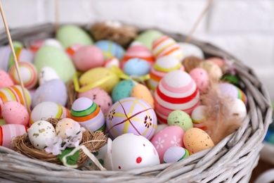 Photo of Many different Easter eggs in wicker basket on light background, closeup