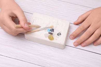 Photo of Child playing with Excavation kit at white wooden table, closeup. Educational toy for motor skills