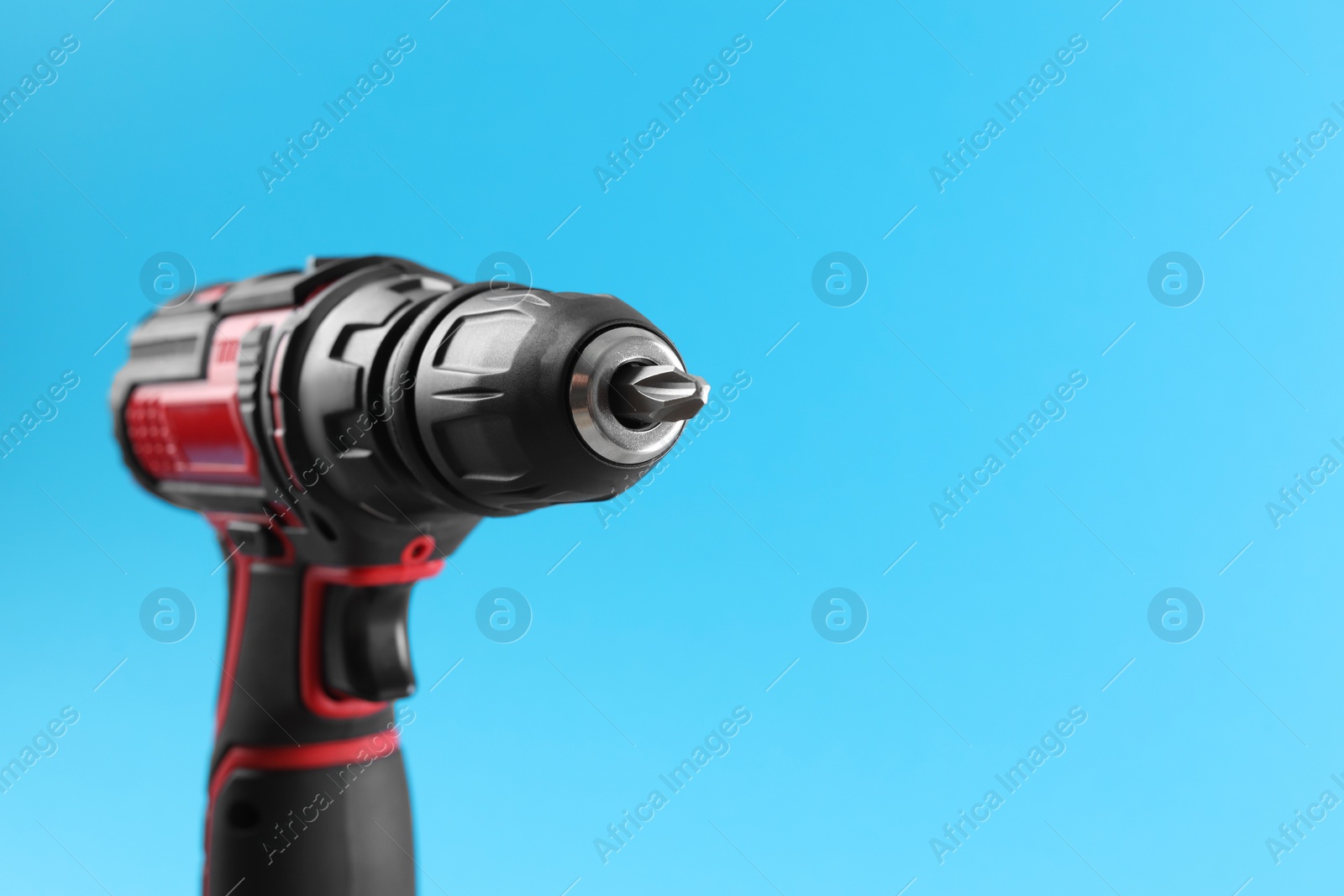 Photo of Modern electric screwdriver on light blue background, closeup. Space for text