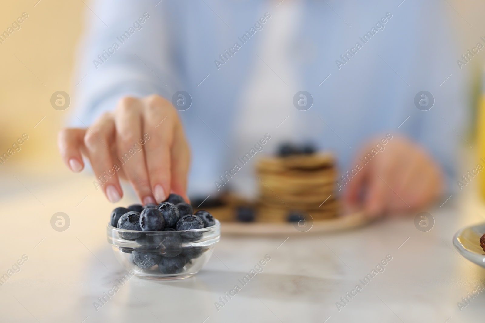 Photo of Woman taking blueberry from glass bowl at table, closeup