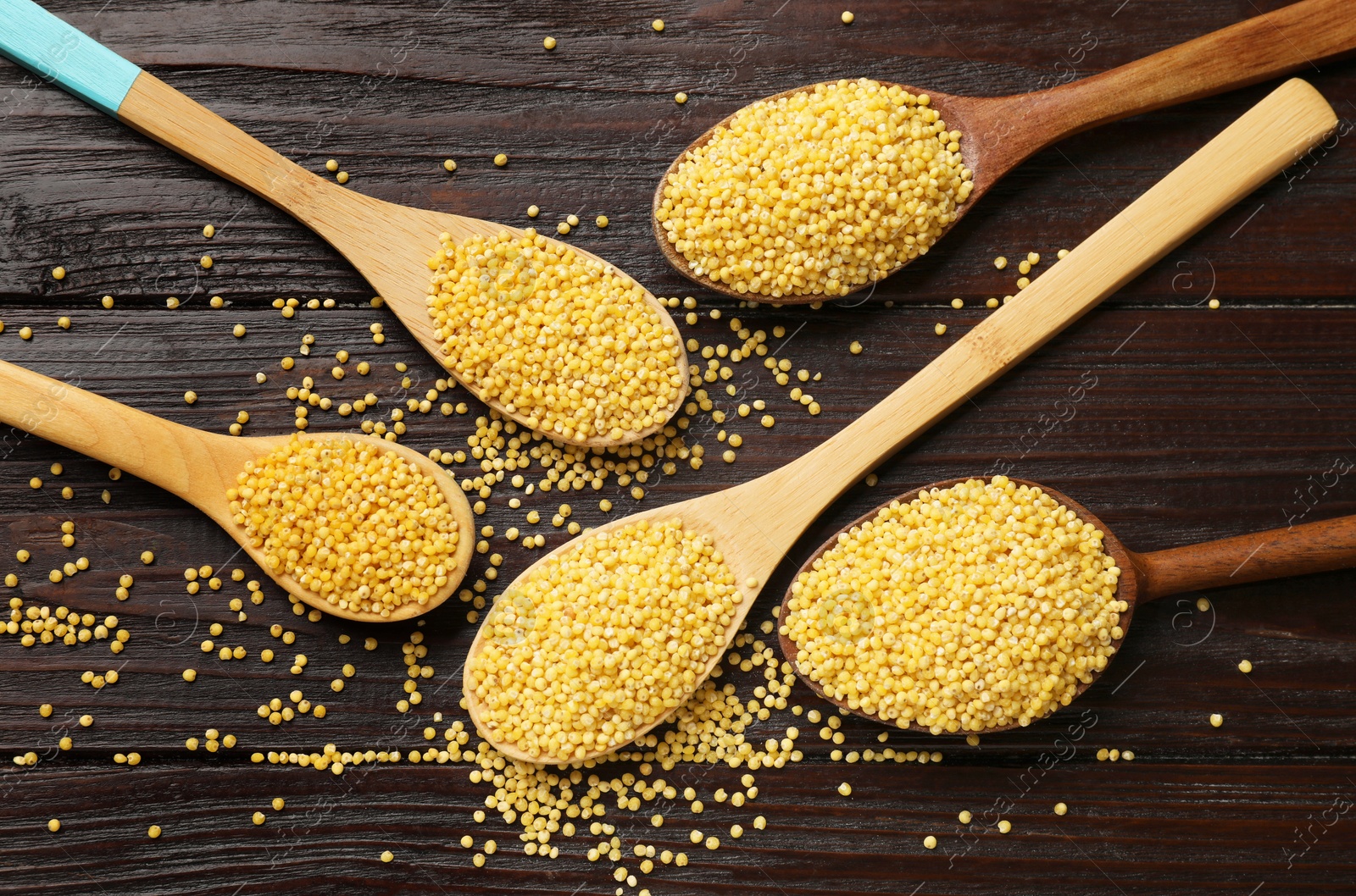 Photo of Spoons with millet groats on wooden table, flat lay