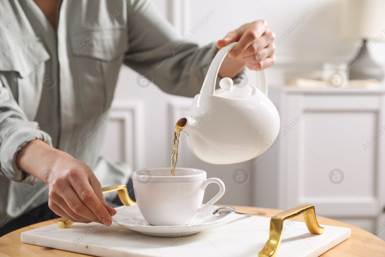 Photo of Woman pouring hot tea into cup at wooden table, closeup