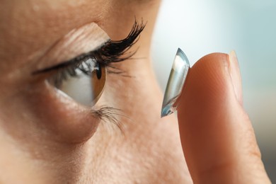 Photo of Young woman putting contact lens in her eye on blurred background, closeup