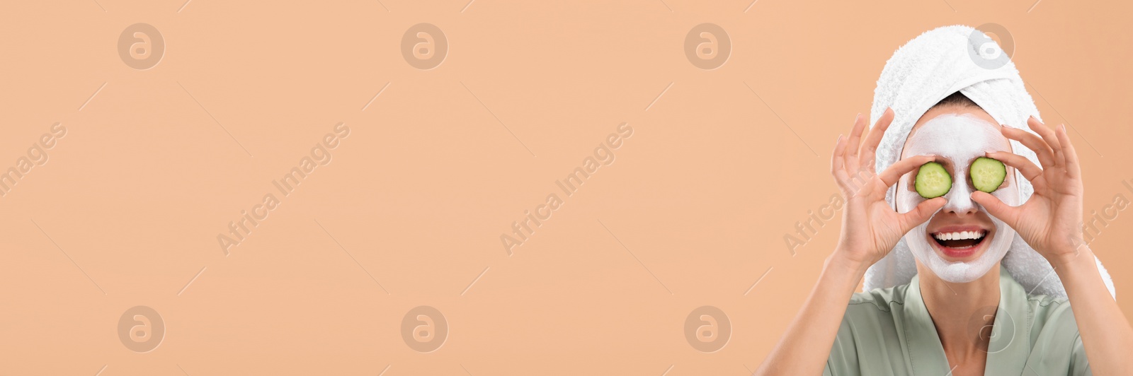 Image of Spa treatment. Happy woman with face mask and cucumber slices on pale orange background. Banner design with space for text
