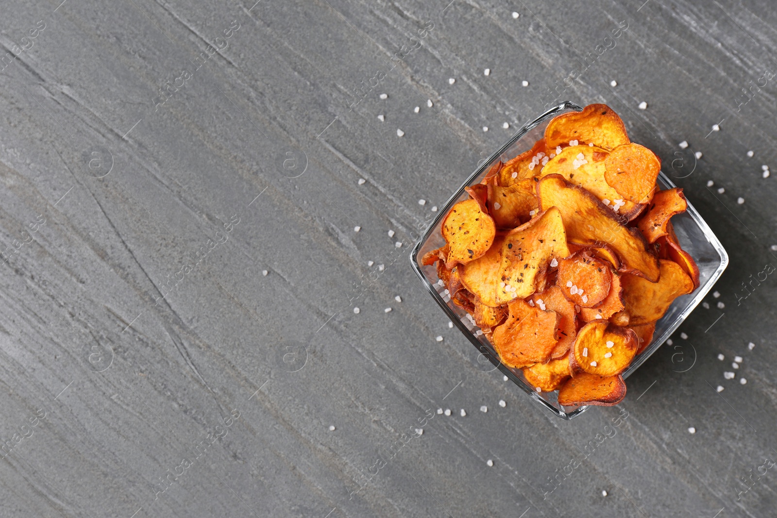 Photo of Bowl of sweet potato chips and salt on grey table, top view. Space for text