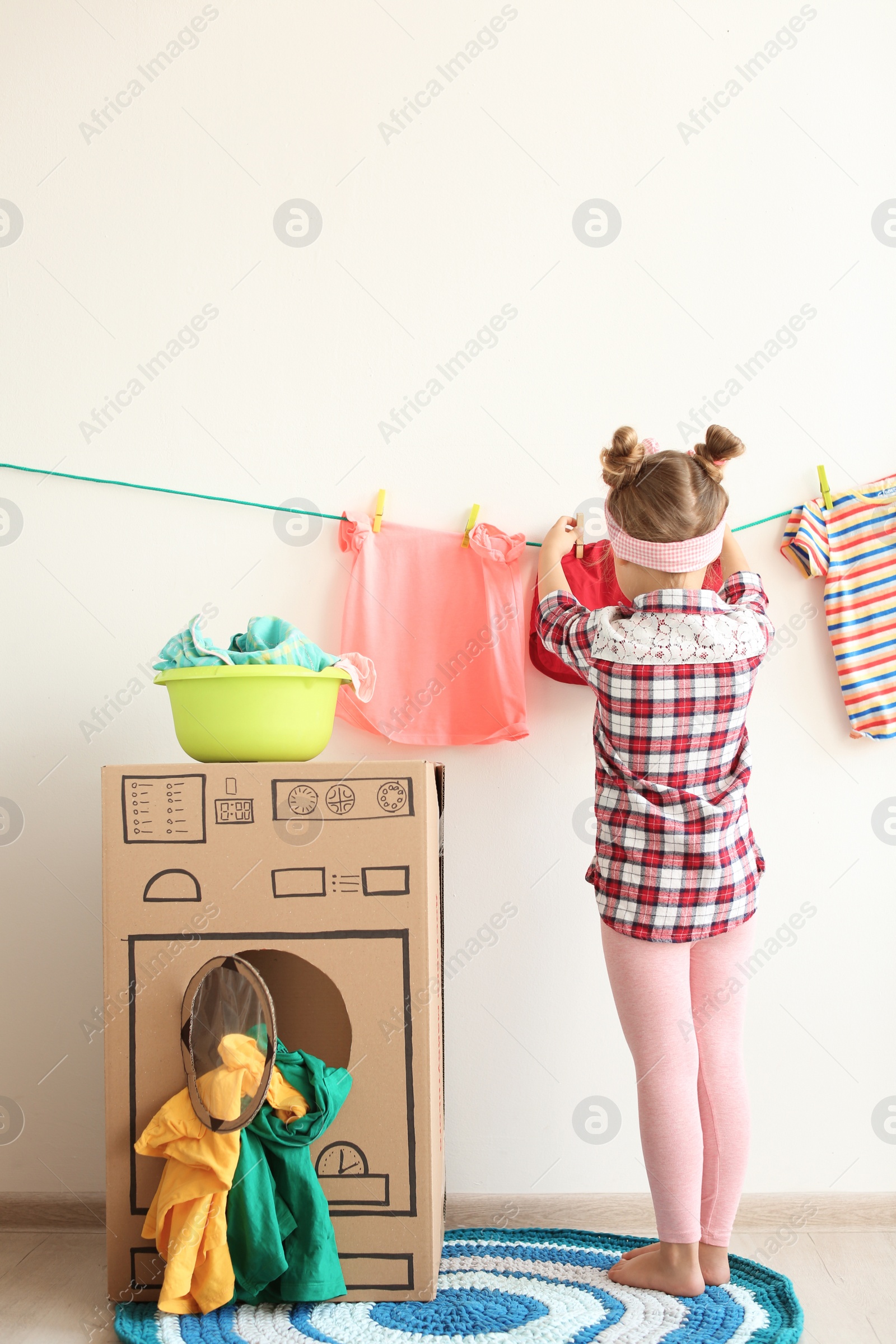 Photo of Adorable little child playing with cardboard washing machine and clothes indoors