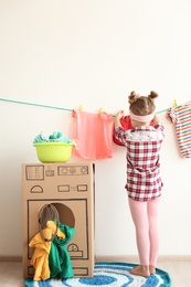 Adorable little child playing with cardboard washing machine and clothes indoors