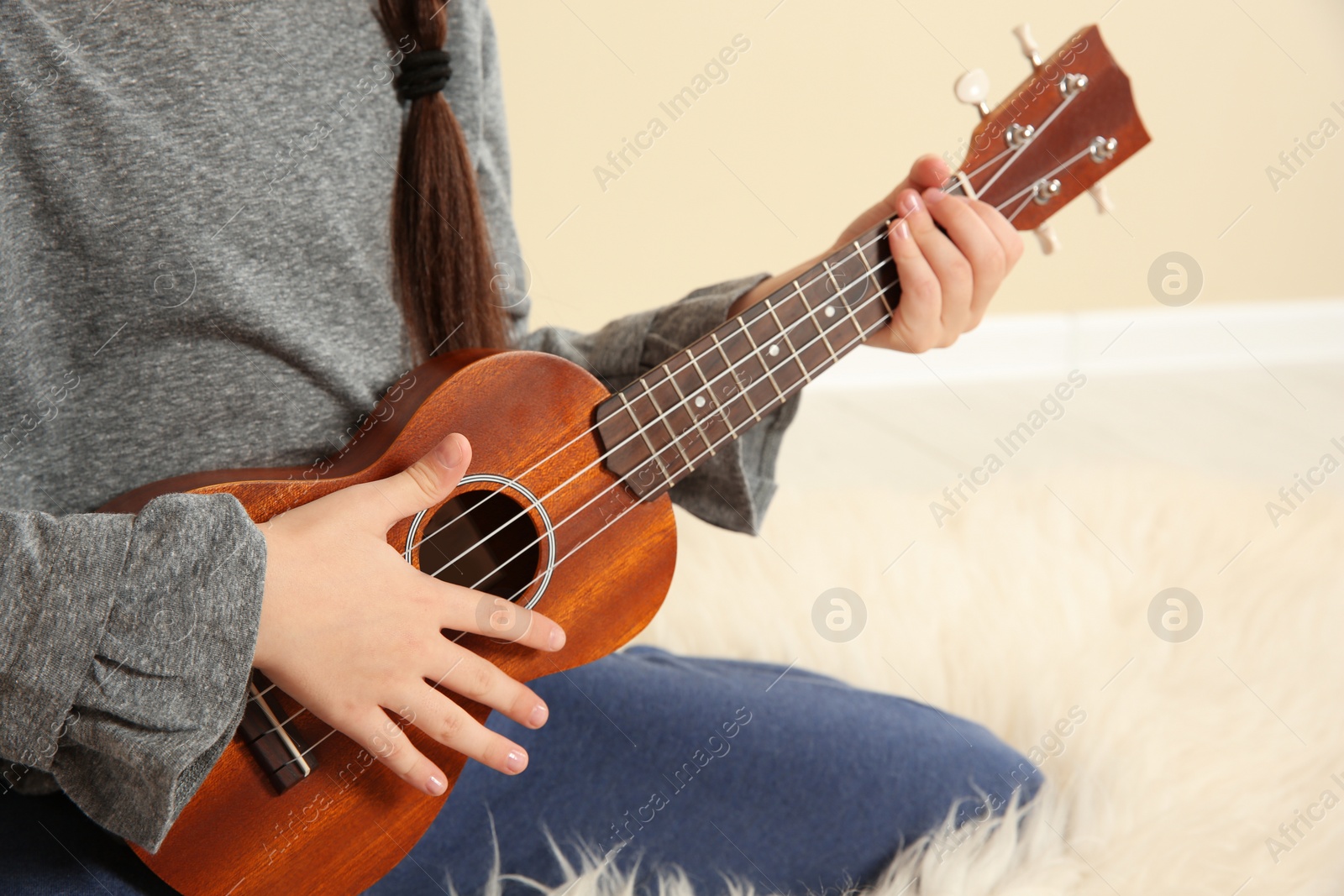 Photo of Little girl playing wooden guitar indoors, closeup