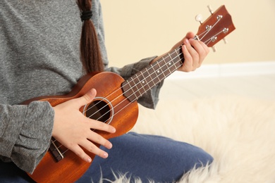 Little girl playing wooden guitar indoors, closeup