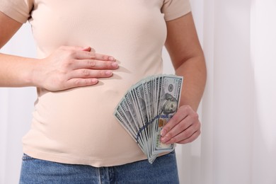 Photo of Surrogate mother. Pregnant woman with dollar banknotes indoors, closeup