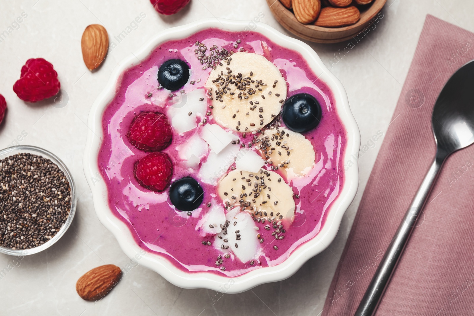 Photo of Delicious acai smoothie with fruits and coconut chips in dessert bowl served on grey table, flat lay