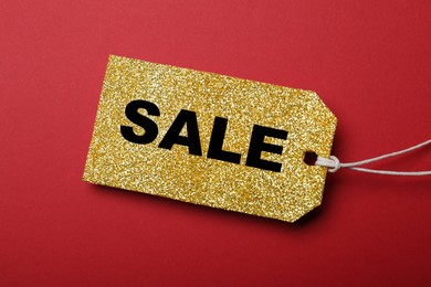 Photo of Golden tag with word Sale on red background, top view. Black Friday