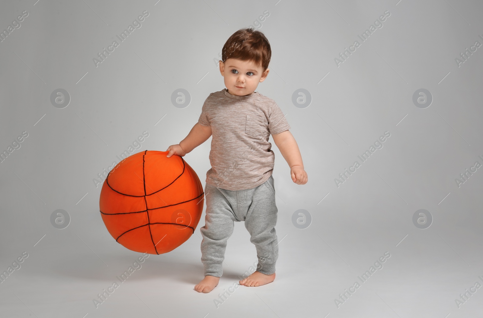 Photo of Cute baby learning to walk and playing on grey background