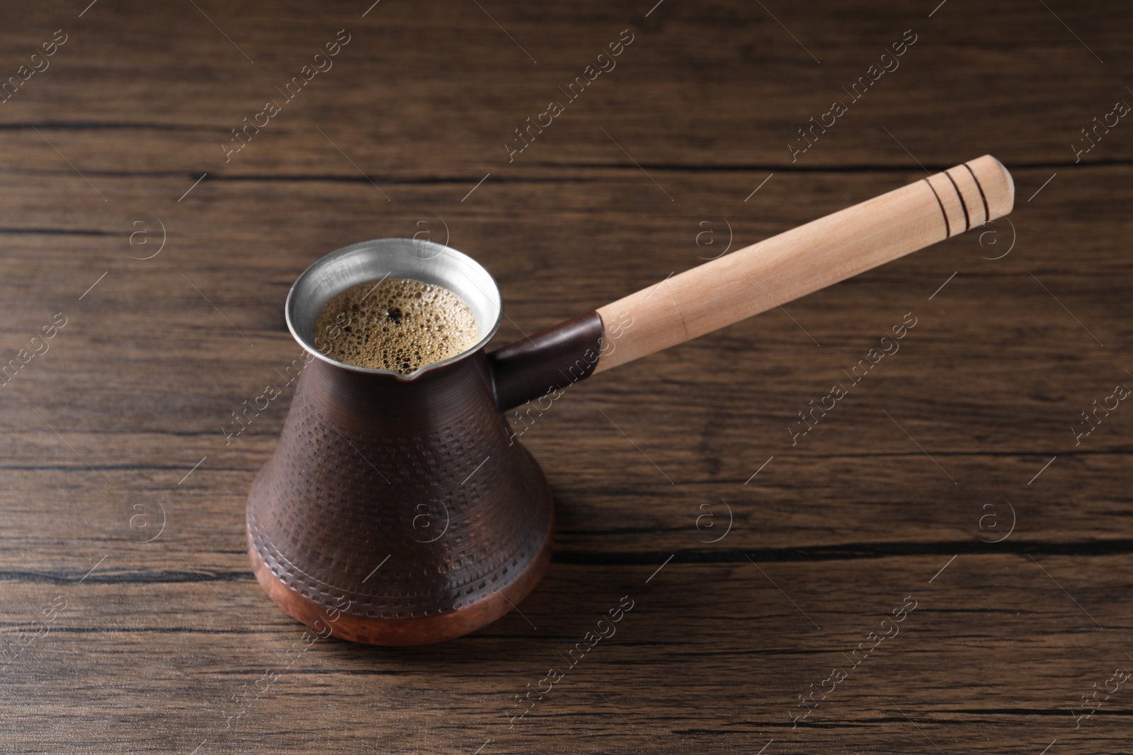 Photo of Turkish coffee in cezve on wooden table