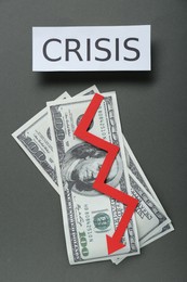 Photo of Paper sheet with word Crisis, money and descending red arrow on grey background, flat lay