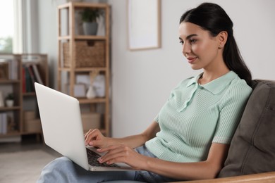 Photo of Young woman working with laptop in armchair at home