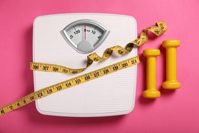 Photo of Weight loss concept. Scales, dumbbells and measuring tape on pink background, flat lay