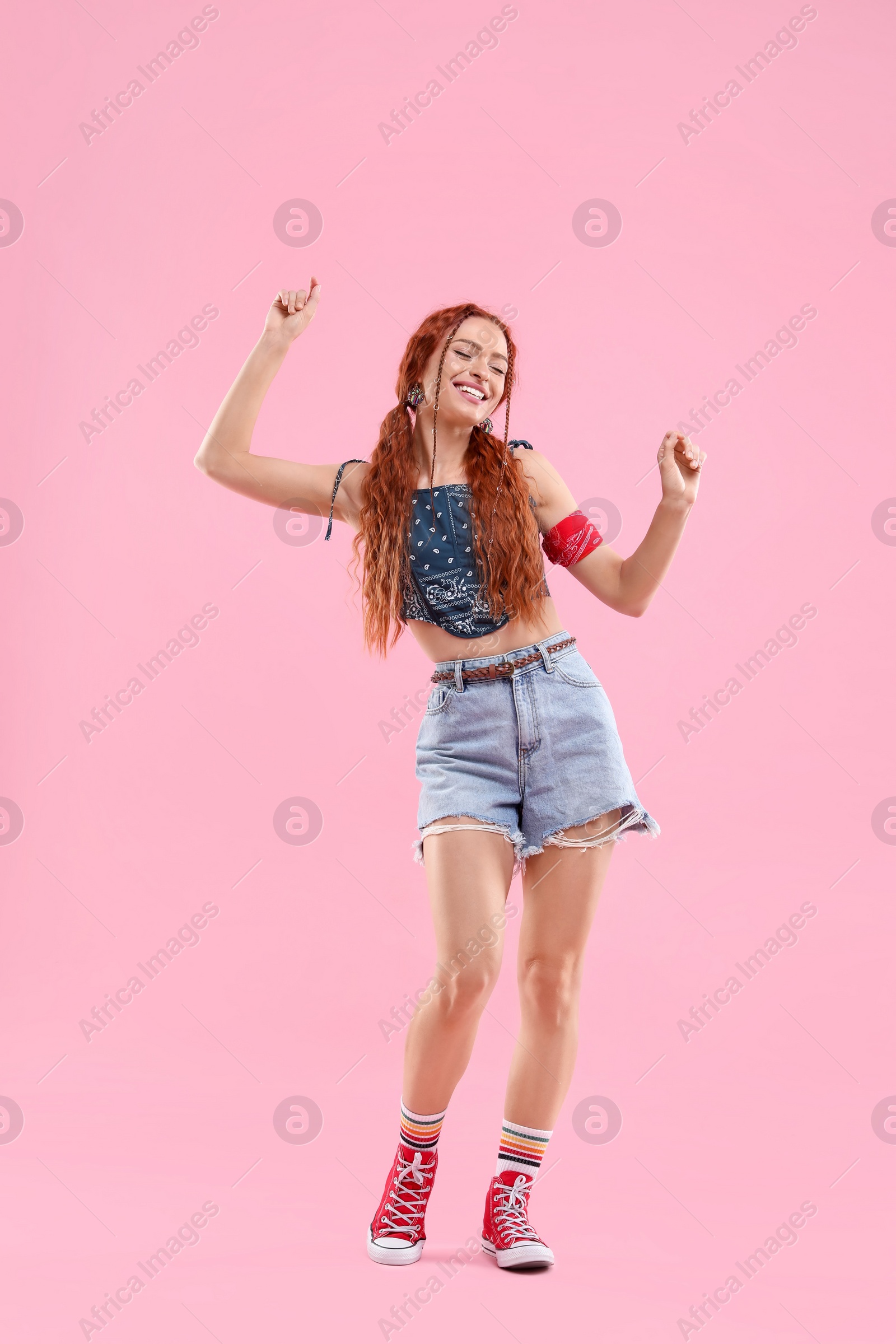 Photo of Stylish young hippie woman dancing on pink background