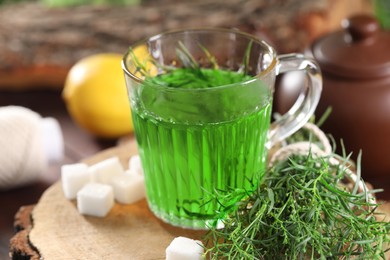 Photo of Aromatic herbal tea, fresh tarragon sprigs and sugar cubes on table, closeup