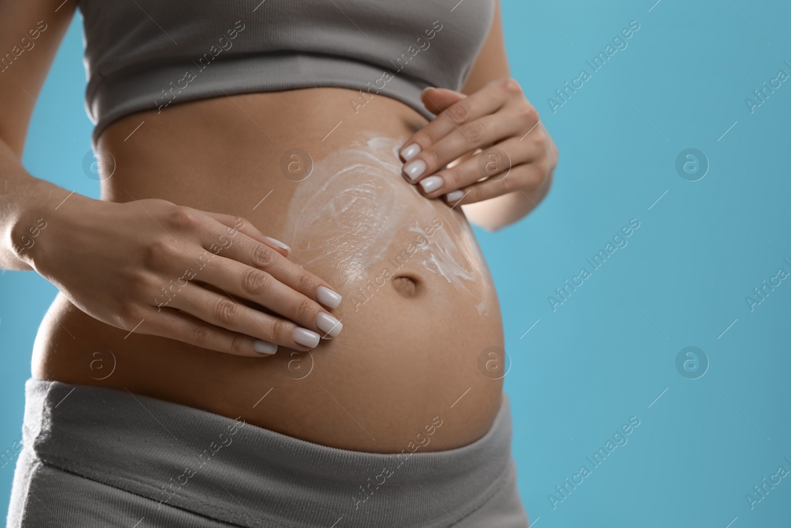 Photo of Pregnant woman applying cosmetic product on belly against light blue background, closeup. Space for text